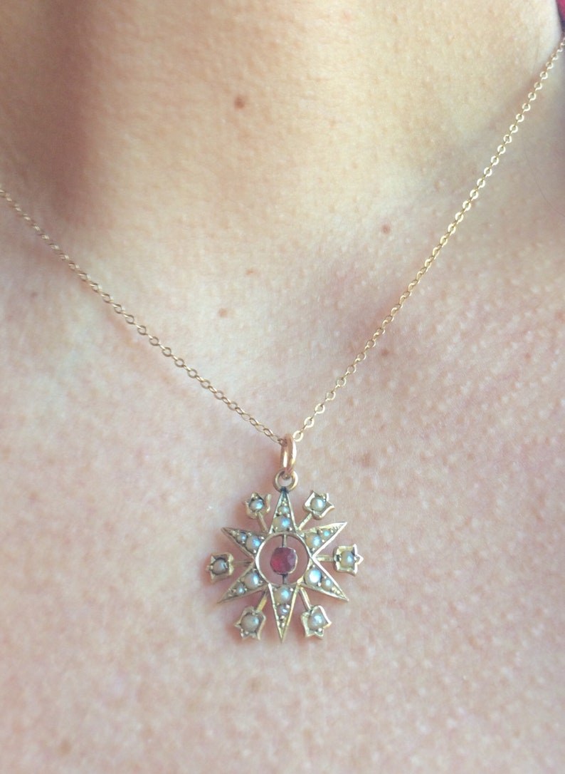 May include: A gold necklace with a star-shaped pendant. The pendant is decorated with small white pearls and a red gemstone in the center.