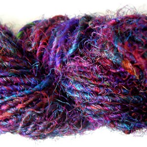Peut inclure: Une pelote de fil color&eacute; avec un m&eacute;lange de teintes violettes, bleues et rouges. Le fil est en soie et a un aspect duveteux et textur&eacute;.