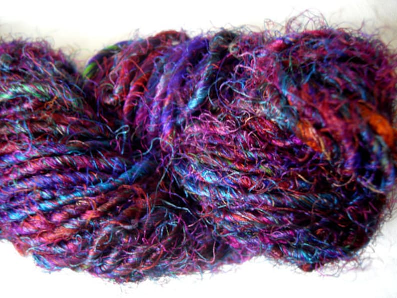 Peut inclure: Une pelote de fil color&eacute; avec un m&eacute;lange de teintes violettes, bleues et rouges. Le fil est en soie et a un aspect duveteux et textur&eacute;.