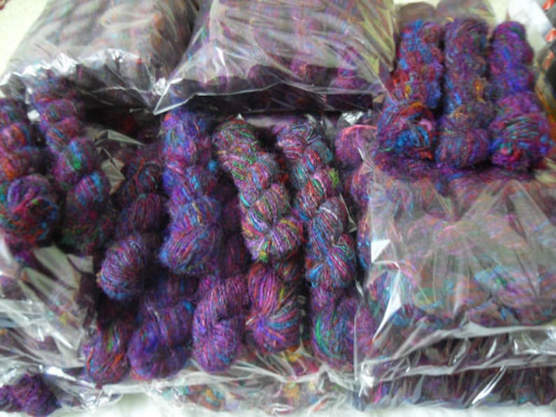 Peut inclure: Plusieurs paquets de fil color&eacute; dans des tons de violet, bleu et vert sont emball&eacute;s dans des sacs en plastique transparent. Le fil est fait d'un mat&eacute;riau doux et duveteux et est parfait pour le tricot ou le crochet.