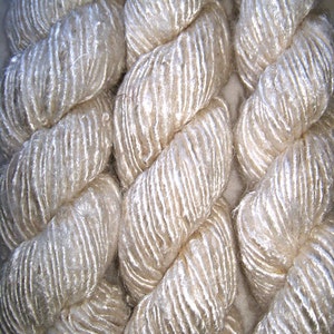 May include: Close-up of a white, silky yarn, twisted into a rope-like shape. The yarn has a subtle sheen and a soft, fluffy texture.