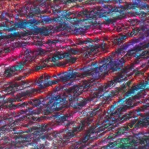 May include: Close-up of a colorful yarn made of various shades of blue, red, pink, and green. The yarn is textured and has a slightly fuzzy appearance.