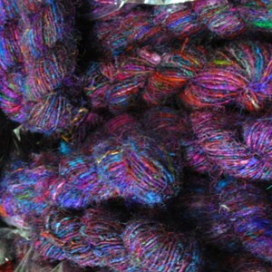 Peut inclure: Gros plan sur un tas de fils color&eacute;s, principalement violets, bleus et rouges, avec quelques accents verts et dor&eacute;s. Le fil est compos&eacute; de diverses fibres, dont la soie et la laine.