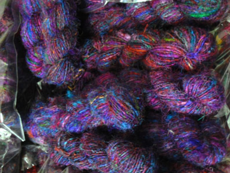 Peut inclure: Gros plan sur un tas de fils color&eacute;s, principalement violets, bleus et rouges, avec quelques accents verts et dor&eacute;s. Le fil est compos&eacute; de diverses fibres, dont la soie et la laine.