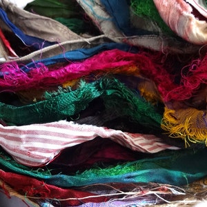 Op de afbeelding: Een close-up van een bundel kleurrijke stoffenresten met rafelige randen. De stof is in verschillende tinten groen, rood, roze, blauw, geel en wit. De stof is in een willekeurig patroon gerangschikt, waardoor een visueel aantrekkelijke en textuurrijke weergave ontstaat.