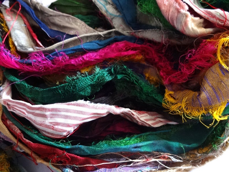 Op de afbeelding: Een close-up van een bundel kleurrijke stoffenresten met rafelige randen. De stof is in verschillende tinten groen, rood, roze, blauw, geel en wit. De stof is in een willekeurig patroon gerangschikt, waardoor een visueel aantrekkelijke en textuurrijke weergave ontstaat.