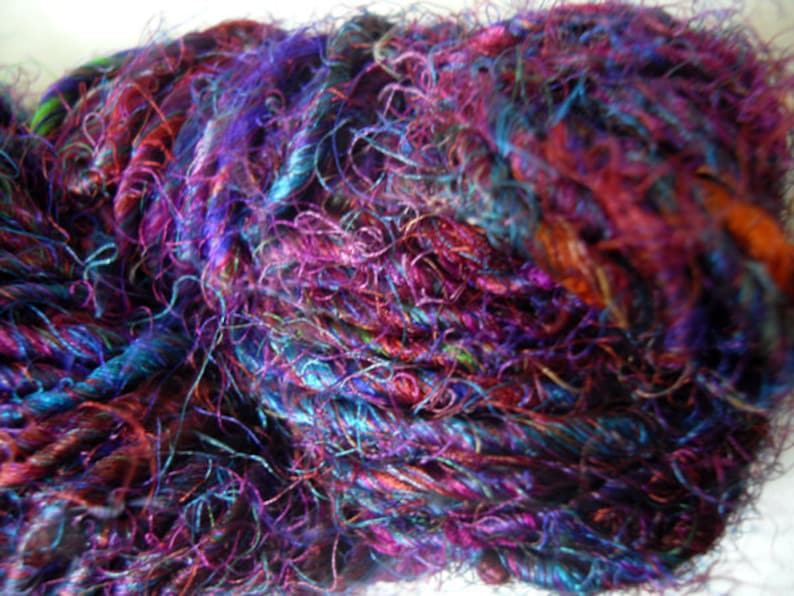 Peut inclure: Un gros plan d'une pelote de fil avec un m&eacute;lange de couleurs violettes, bleues et brunes. Le fil est tr&egrave;s fin et a une texture duveteuse.