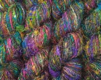Könnte beinhalten: Nahaufnahme eines Bündels bunter Garne mit verschiedenen Texturen. Das Garn ist eine Mischung aus Grün, Blau, Lila und Braun.