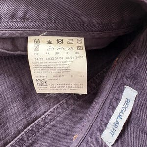 Puede incluir: Primer plano de unos vaqueros morados con una etiqueta que muestra las instrucciones de lavado y la informaci&oacute;n de la talla. La etiqueta tambi&eacute;n incluye el texto "REGULAR FIT".