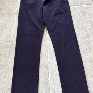 Puede incluir: Vaqueros de mezclilla azul marino oscuro con bragueta de botones. Los vaqueros est&aacute;n colocados planos sobre una alfombra de color claro. Los vaqueros tienen un dise&ntilde;o cl&aacute;sico de cinco bolsillos y corte recto.