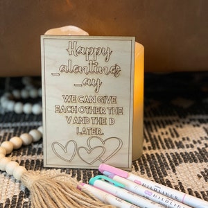 Puede incluir: Un letrero de madera con el texto "Happy Valentines-ay WE CAN GIVE EACH OTHER THE V AND THE D LATER." El letrero tiene tres corazones dibujados en &eacute;l.