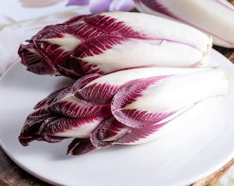 May include: Two red and white radicchio heads on a white plate. The radicchio is a type of chicory with a slightly bitter flavor.