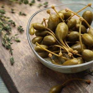 a glass bowl filled with green olives on top of a wooden cutting board