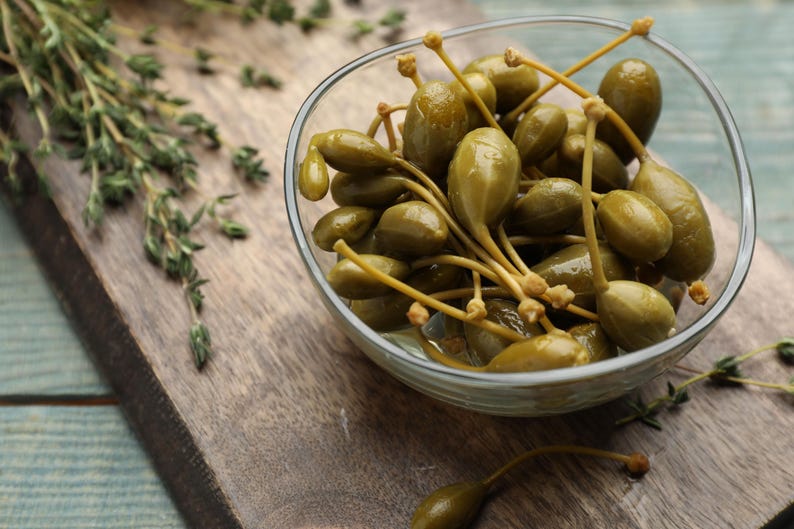 a glass bowl filled with green olives on top of a wooden cutting board