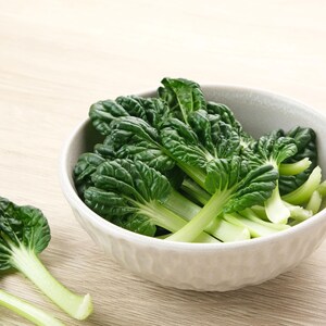 a bowl filled with green leafy vegetables on top of a wooden table