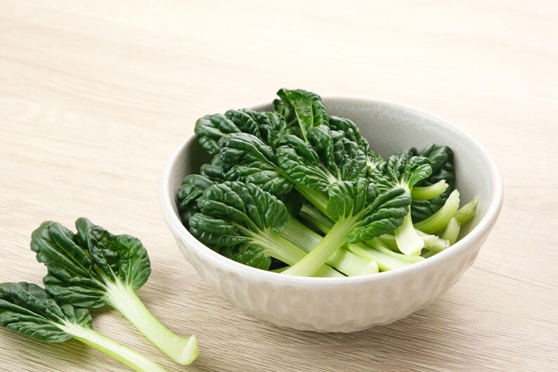 a bowl filled with green leafy vegetables on top of a wooden table