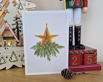 May include: A Christmas card with a gold star design, a candle flame, and green pine branches. The card is displayed with a wooden Christmas tree, a nutcracker, and a calendar showing the date December 25.