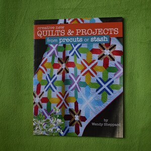 May include: Book cover with the title "Creative New Quilts & Projects from Precuts or Stash" by Wendy Sheppard. The cover features a colorful quilt with a geometric pattern.