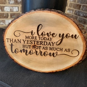 May include: Wooden slice with the text "i love you more today than yesterday but not as much as tomorrow" burned into the surface.
