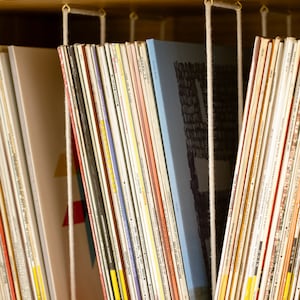 Puede incluir: Una estanter&iacute;a con una variedad de libros coloridos organizados por color y mantenidos en su lugar por cordones blancos. Los libros est&aacute;n dispuestos en una pila vertical y son de diferentes tama&ntilde;os y formas.