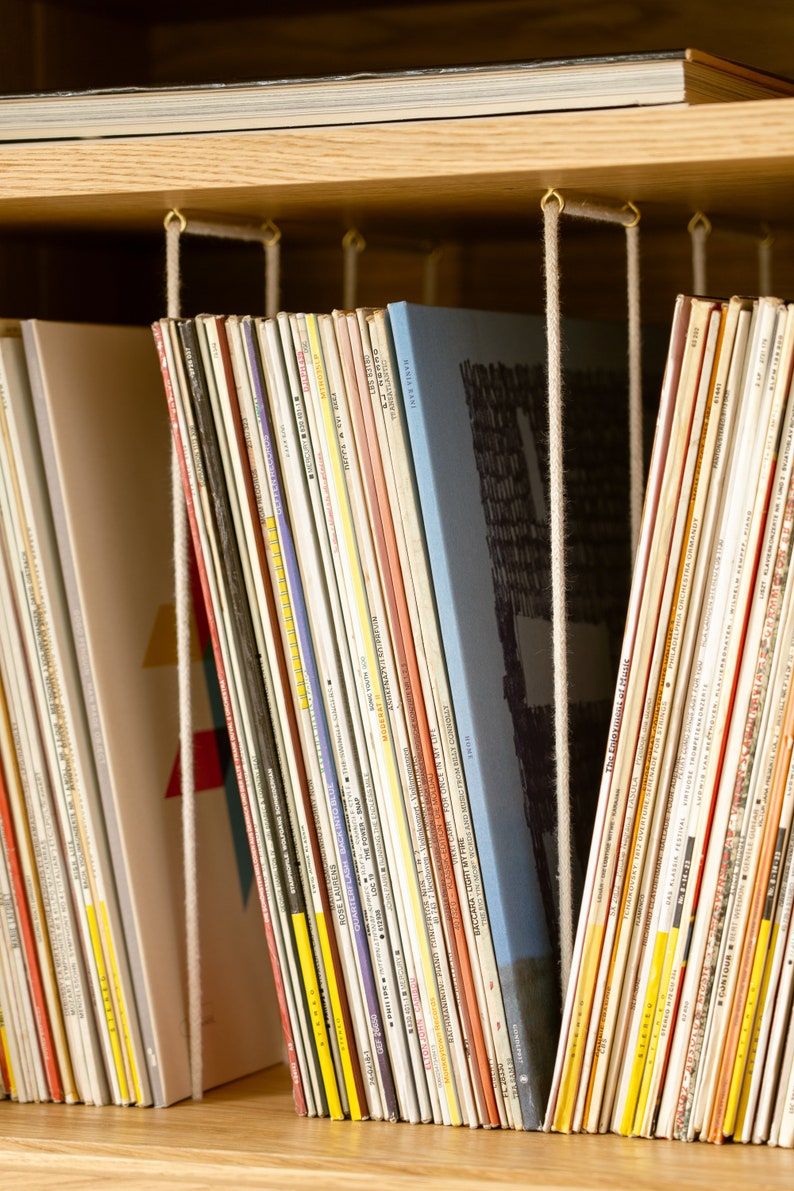 Puede incluir: Una estanter&iacute;a con una variedad de libros coloridos organizados por color y mantenidos en su lugar por cordones blancos. Los libros est&aacute;n dispuestos en una pila vertical y son de diferentes tama&ntilde;os y formas.