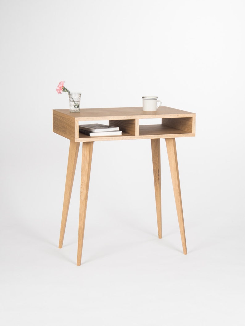 May include: A light wood table with a shelf and tapered legs. A pink flower in a glass vase and a white mug are on the table.