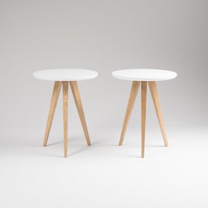 May include: Two white round side tables with wooden legs. The tables are on a white background.