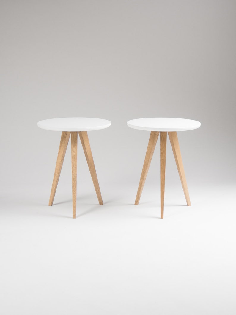 May include: Two white round side tables with wooden legs. The tables are on a white background.