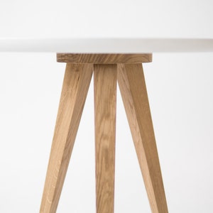 May include: A white round table with a wooden tripod base. The table top is smooth and the legs are made of natural wood.
