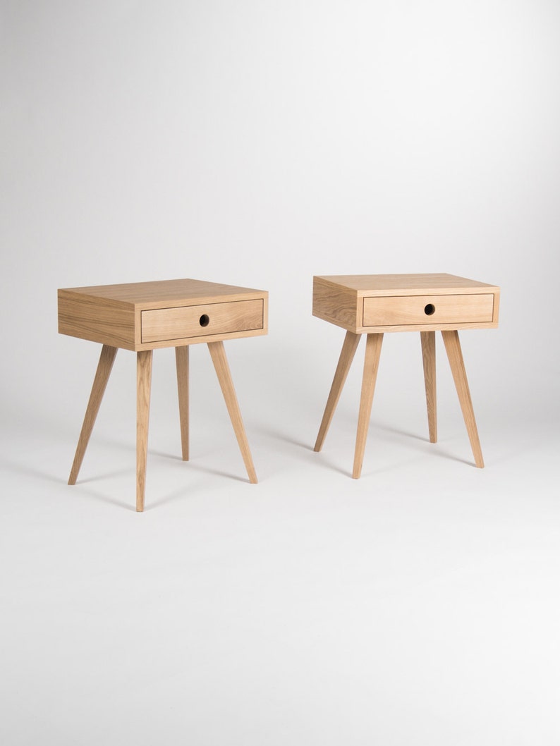 May include: Two wooden bedside tables with a single drawer and four legs. The tables are made of light wood and have a simple, modern design.