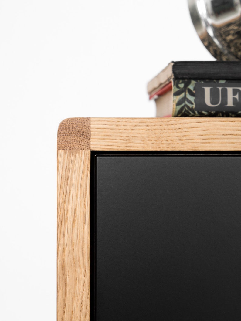 May include: Close-up of a wooden cabinet with a black door. The cabinet has a natural wood finish and a mitered corner detail. The door is made of a smooth, black material.