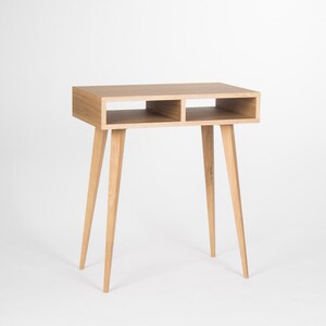 May include: A light wood desk with two open shelves and four tapered legs. The desk is made of solid wood and has a natural finish.