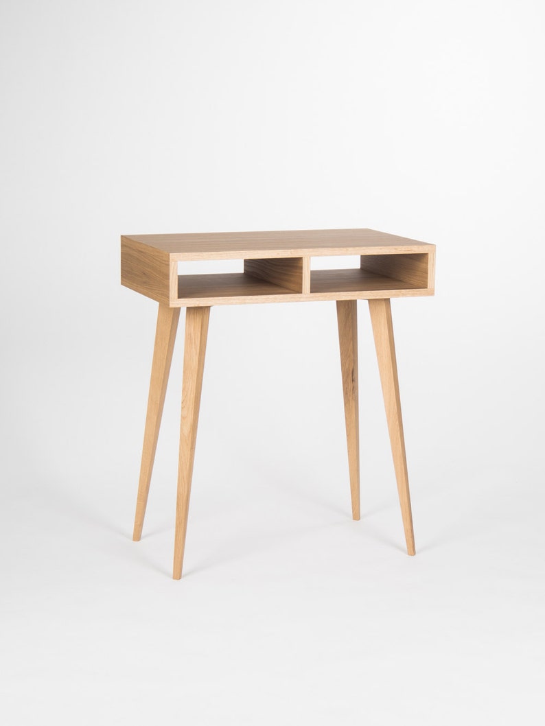 May include: A light wood desk with two open shelves and four tapered legs. The desk is made of solid wood and has a natural finish.