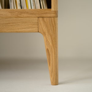Puede incluir: Primer plano de la parte inferior de un mueble de discos de madera con un caj&oacute;n y patas c&oacute;nicas.