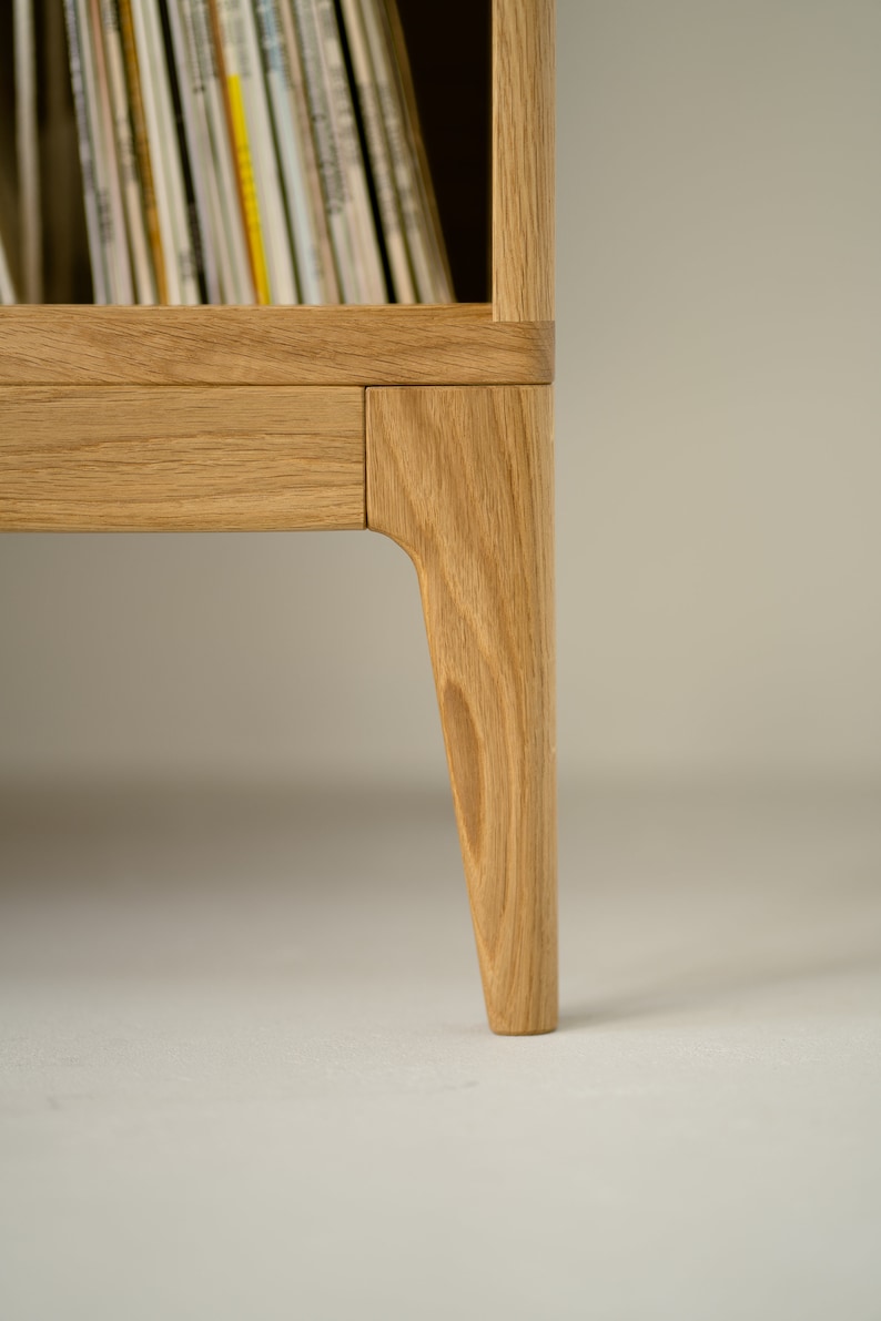 Puede incluir: Primer plano de la parte inferior de un mueble de discos de madera con un caj&oacute;n y patas c&oacute;nicas.
