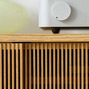 Puede incluir: Un armario de madera clara con listones verticales y un amplificador plateado con una perilla de volumen en la parte superior.