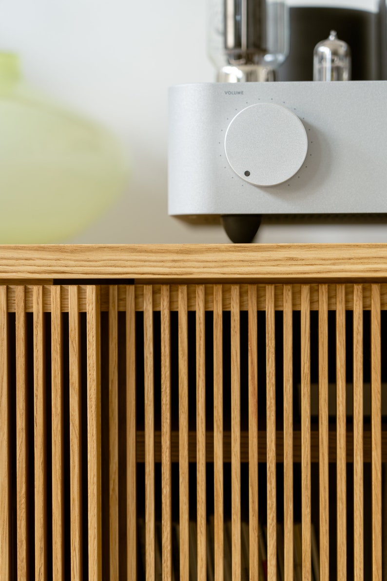 Puede incluir: Un armario de madera clara con listones verticales y un amplificador plateado con una perilla de volumen en la parte superior.