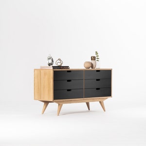 May include: A six-drawer dresser with black drawers and a light wood frame. The dresser has tapered legs and is sitting on a white surface.