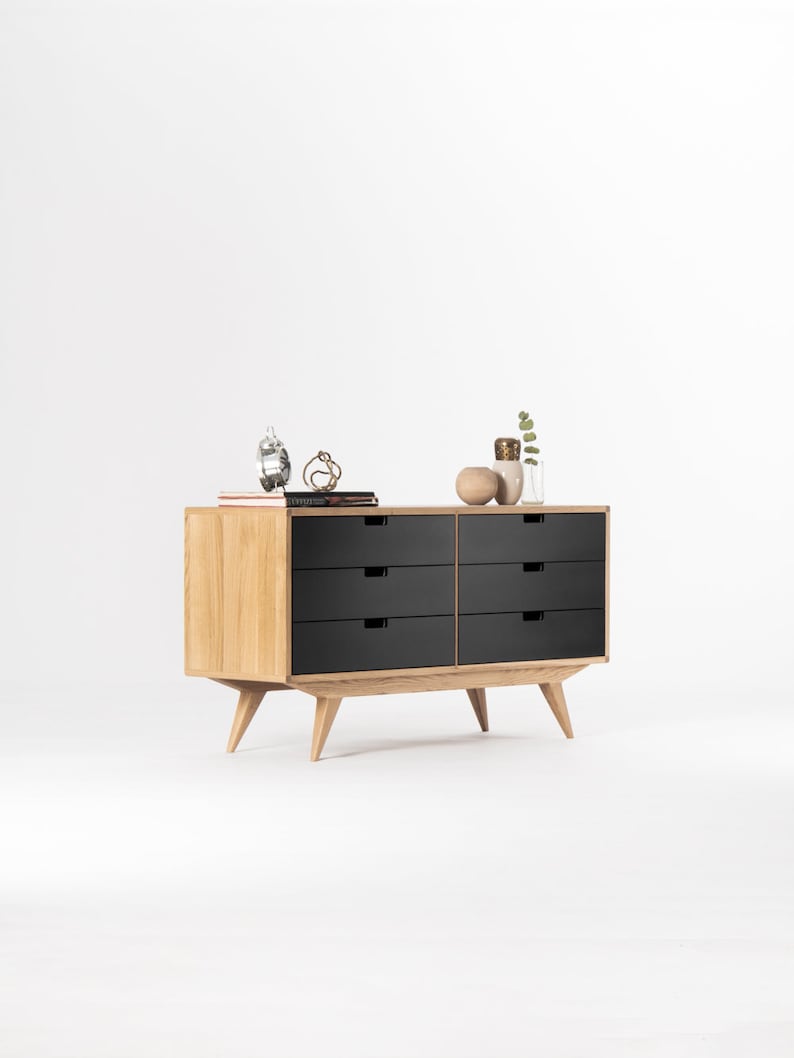 May include: A six-drawer dresser with black drawers and a light wood frame. The dresser has tapered legs and is sitting on a white surface.