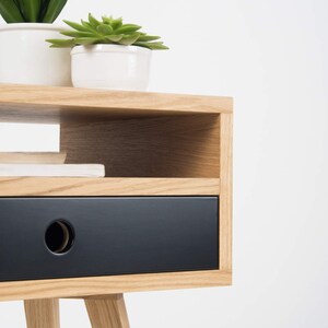 Puede incluir: Una mesita de noche de madera con un caj&oacute;n negro y un estante. La mesita de noche tiene un dise&ntilde;o sencillo con patas c&oacute;nicas.