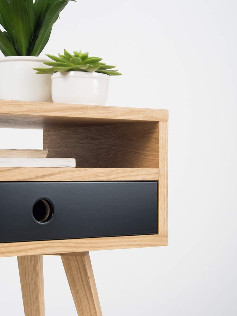 Puede incluir: Una mesita de noche de madera con un caj&oacute;n negro y un estante. La mesita de noche tiene un dise&ntilde;o sencillo con patas c&oacute;nicas.