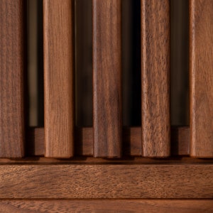May include: Close-up of a wooden slat wall with a dark brown stain. The slats are arranged vertically and are evenly spaced. The wood has a natural grain pattern.
