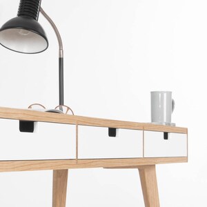 Puede incluir: Un escritorio blanco con tres cajones y patas de roble. El escritorio tiene un dise&ntilde;o simple y moderno y es perfecto para una oficina en casa o un estudio.