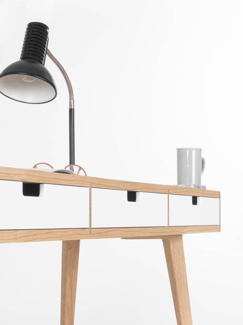 Puede incluir: Un escritorio blanco con tres cajones y patas de roble. El escritorio tiene un dise&ntilde;o simple y moderno y es perfecto para una oficina en casa o un estudio.