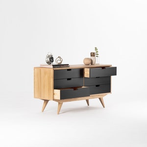 May include: A six-drawer dresser with a light wood frame and black drawers. The dresser has a mid-century modern design with tapered legs.