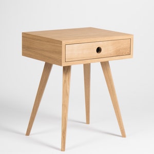 May include: A light wood bedside table with a single drawer and four tapered legs. The drawer has a round cutout for a handle.