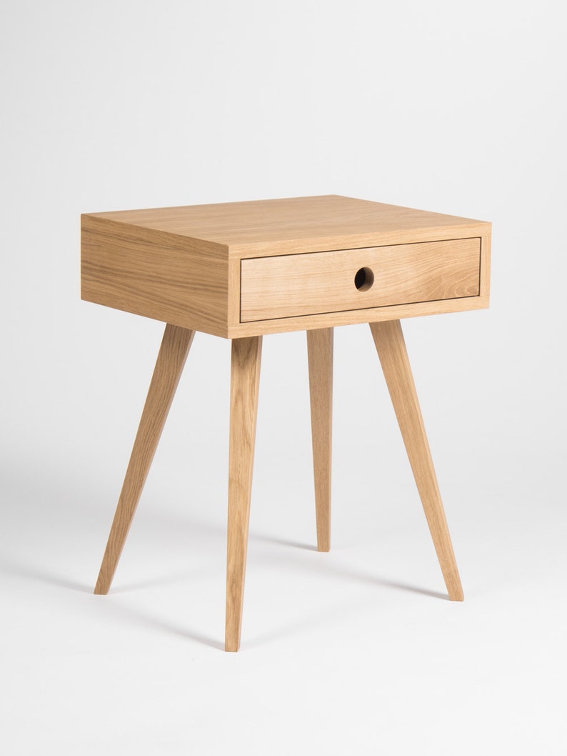 May include: A light wood bedside table with a single drawer and four tapered legs. The drawer has a round cutout for a handle.