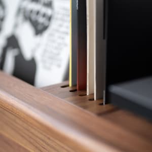 May include: Close-up of a wooden record shelf with several vinyl records inserted into the slots. The records are various colors, including black, white, and yellow.