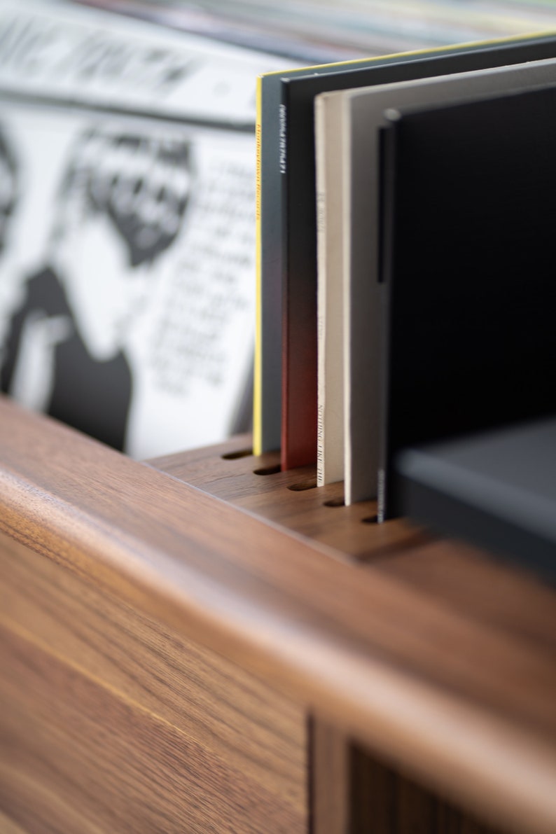 May include: Close-up of a wooden record shelf with several vinyl records inserted into the slots. The records are various colors, including black, white, and yellow.