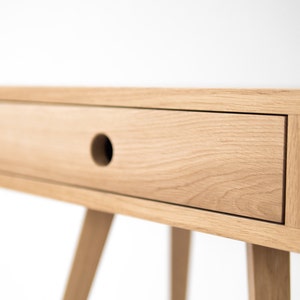 May include: A light wood bedside table with a single drawer and tapered legs. The drawer has a round cutout for a handle.